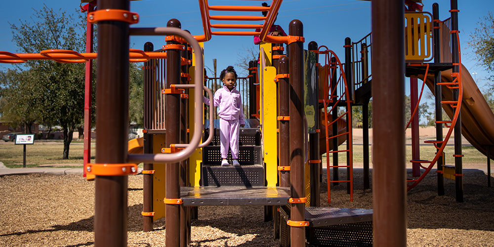 Child stands inside jungle gym feature at a park playground.